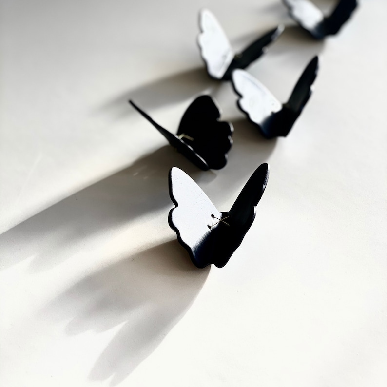 May include: A row of black butterfly-shaped paper clips on a white surface.