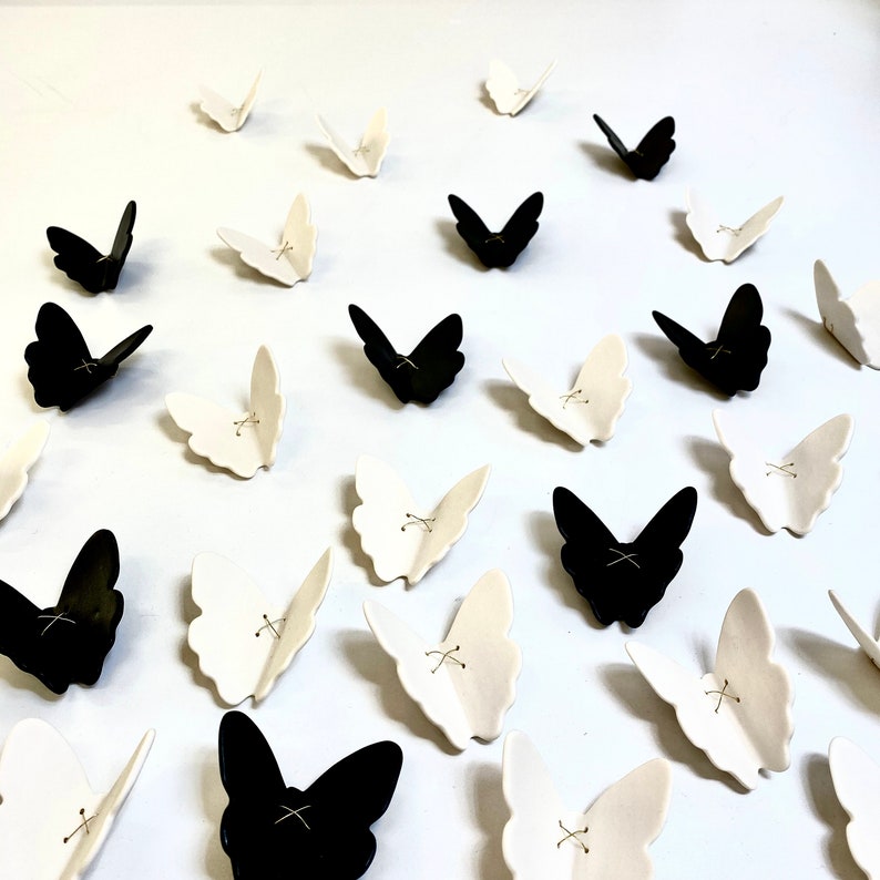 May include: A collection of black and white ceramic butterflies. The butterflies are arranged in a random pattern on a white surface.