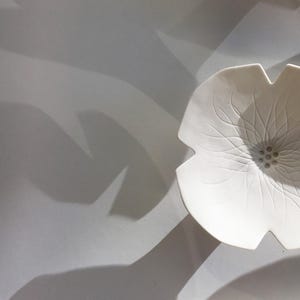 Może przedstawiać: Biała ceramiczna miska z wzorem kwiatu. Miska ma wypukłe centrum z małym k&oacute;łkiem kropek.