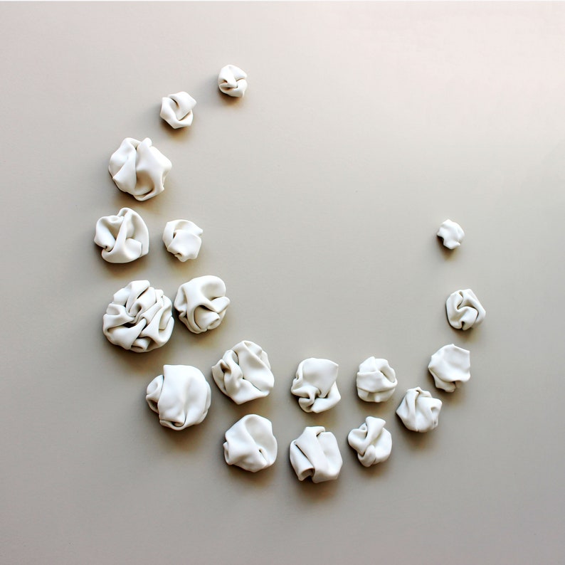 Set of 18 ceramic sculptures arranged in a crescent moon shape. Each individual piece is a unique creation featuring lots of curves and folds that have formed naturally when the clay has been warped in my hands.