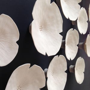 Close up of white porcelain ceramic flowers. The image shows the sculpture wall art from the side so you can see the ceramic stem at the back. This is how they attach to the wall.