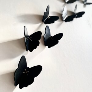 May include: Black butterfly wall decor with a simple, minimalist design. Each butterfly has a small gold accent in the center.