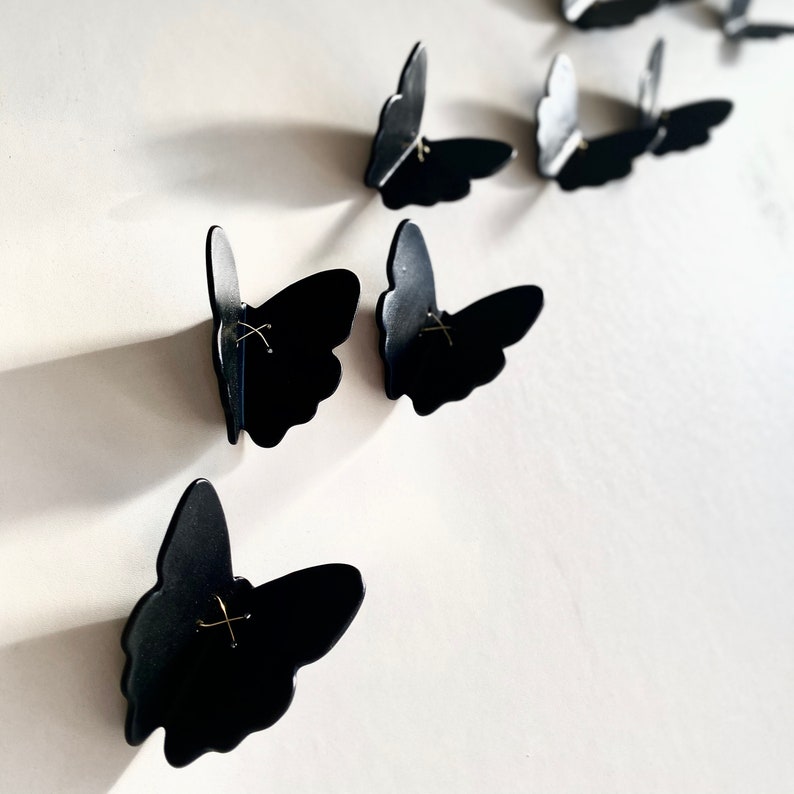 May include: Black butterfly wall decor with a simple, minimalist design. Each butterfly has a small gold accent in the center.