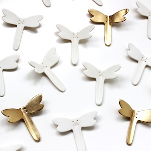 Original artwork, a close up of porcelain ceramic dragonfly sculptures. Minimalist design white and gold wall art dragonflies. Designed to flutter along your interior walls.