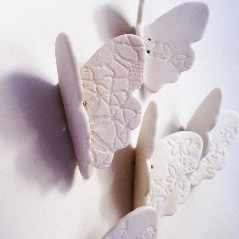 May include: Five white ceramic butterflies with intricate embossed designs. The butterflies are arranged in a cluster, with their wings overlapping.