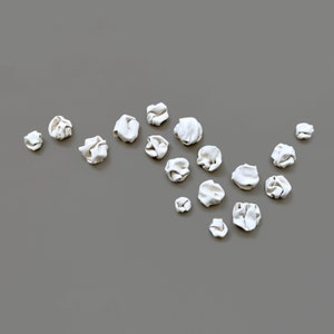 The same sculpture set of 18 pieces arranged in a different composition. This art composition is an organic floaty line with a dense featuring more pieces positioned closer together. This unique porcelain ceramic wall art is designed for interiors.