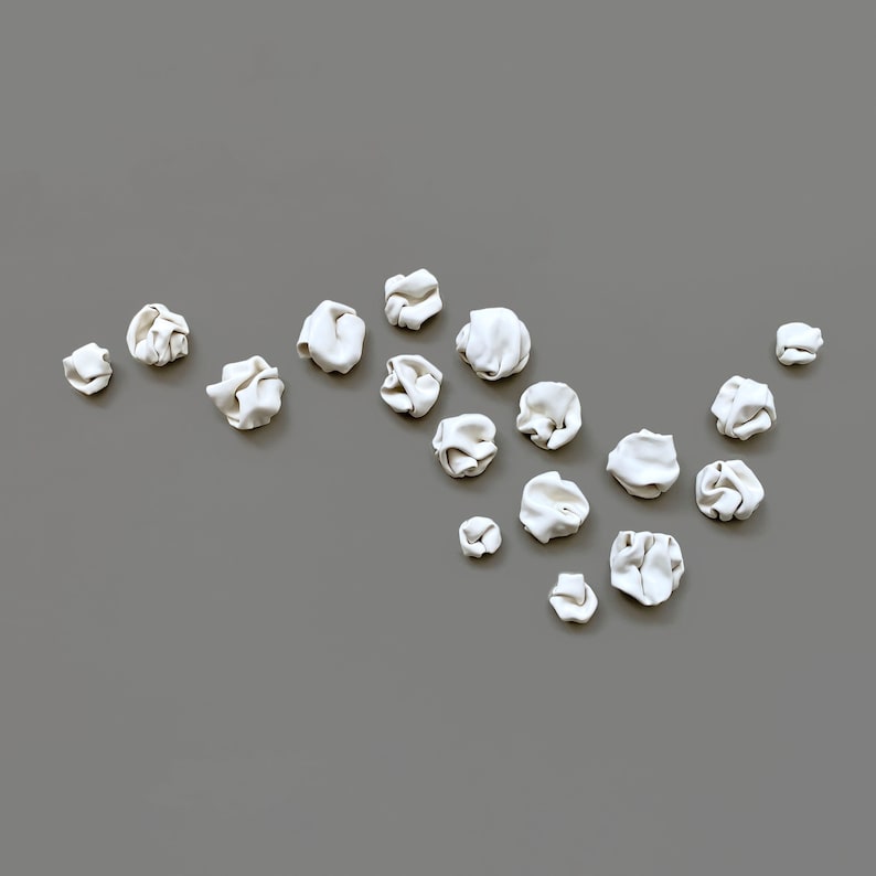 The same sculpture set of 18 pieces arranged in a different composition. This art composition is an organic floaty line with a dense featuring more pieces positioned closer together. This unique porcelain ceramic wall art is designed for interiors.