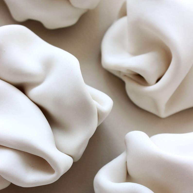 Close up of circular original ceramic wall art. The set is title Flow and the sculptures in the image are formed by organically folding the clay onto itself to create natural curvature and forms. Original abstract artwork.