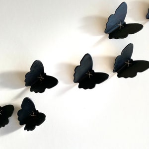 May include: A set of black butterfly wall decor with gold accents. The butterflies are arranged in a staggered pattern on a white background.