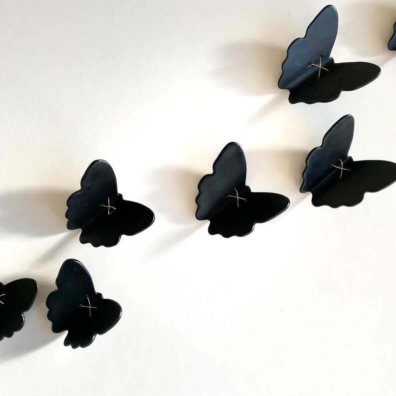 May include: A set of black butterfly wall decor with gold accents. The butterflies are arranged in a staggered pattern on a white background.