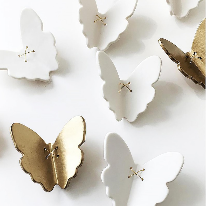 Seven simple porcelain butterflies with golden stitches of wire in the centre, Five are white porcelain and two are gold. They are wall art sculptures to be arranged on the wall and can be arranged in any way that suits the space.
