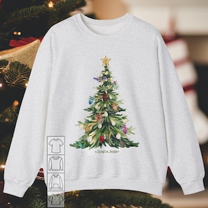 May include: A light gray sweatshirt featuring a watercolor Christmas tree decorated with colorful bugs and a gold star. The text "<Jingle_bugs>" is printed below the tree. The sweatshirt has a crew neck and long sleeves.