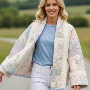 Puede incluir: Una chaqueta acolchada con diseño de patchwork en colores pastel suaves que incluyen rosa claro, azul y crema. La chaqueta tiene un cuello ancho, mangas largas con puños doblados y se lleva sobre una camiseta azul claro y pantalones blancos.