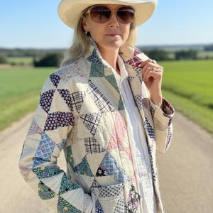 May include: A quilted jacket constructed from various triangular fabric patches in cream, blue, red, and green floral and plaid patterns. The jacket features a high collar, long sleeves, and two front pockets, worn over a plain white collared shirt.