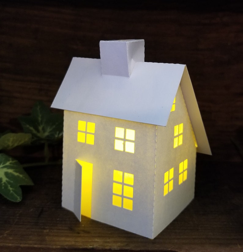 May include: A white paper house with a chimney and windows. The house is lit from inside, creating a warm glow.
