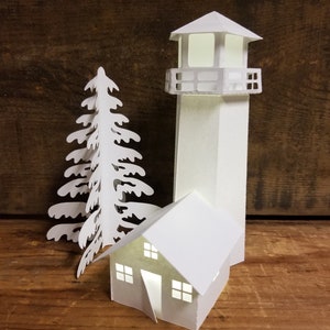 May include: White papercraft model of a lighthouse, a small house, and a pine tree. The lighthouse has a balcony and a window. The house has a door and two windows. The pine tree has a detailed design.