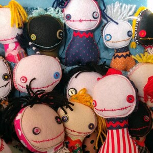 K&ouml;nnte beinhalten: Eine Sammlung handgemachter Stoffpuppen mit verschiedenen Farben, Mustern und Gesichtsz&uuml;gen. Jede Puppe hat Knopfaugen und ein gesticktes L&auml;cheln. Die Puppen sind aus Stoff gefertigt und haben eine skurrile, handgemachte &Auml;sthetik.