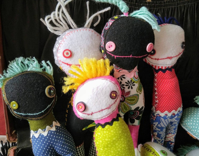 K&ouml;nnte beinhalten: F&uuml;nf handgefertigte Filzpuppen mit verschiedenen Haarfarben und Kleidung. Die Puppen haben Knopfaugen und gen&auml;hte L&auml;cheln.
