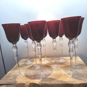 May include: Set of ten clear glass wine glasses with a red tinted bowl. The glasses have a thick, clear stem with a decorative knob at the base.