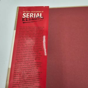 May include: A red book titled "The Visual Encyclopedia of Serial Killers." The cover features white text on a red background. The book explores the psychology and history of serial killers, including profiles of infamous murderers.