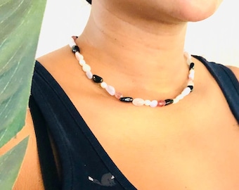 Puede incluir: Primer plano de un collar con cuentas blancas, rosadas y negras. El collar lo lleva una persona con una camiseta sin mangas negra.