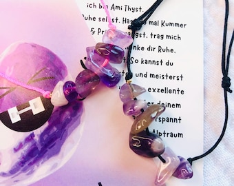 May include: Amethyst crystal necklaces with a black cord and pink string. The necklaces feature polished purple and clear stones. A card with German text is visible in the background, with the word "methyst" at the top.