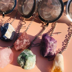 May include: Seven silver tea infusers with chains hanging from them. Each chain has a different colored crystal attached to it: blue, pink, green, purple, and yellow.