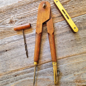 May include: A set of vintage drafting tools including a large wooden compass with brass fittings, a small T-handle hand drill with a metal bit, and a rectangular brass spirit level with a central glass vial and two visible screws.