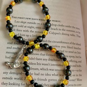 May include: Two beaded bracelets with black, yellow, and orange beads. One bracelet has a silver charm of a hammer, and the other has a saw charm. The word "LEO" is visible in the background.