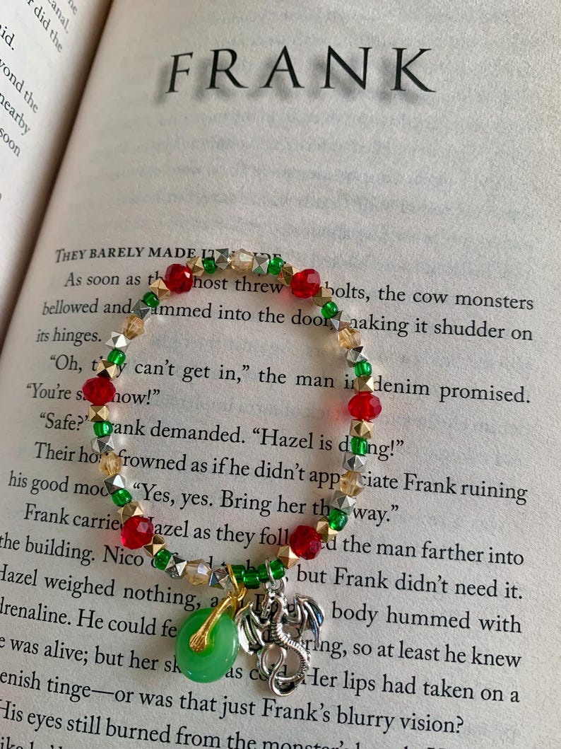May include: A beaded bracelet with red, green, gold, and silver beads. The bracelet features a green jade pendant and a silver dragon charm. The word "FRANK" is visible in the background.