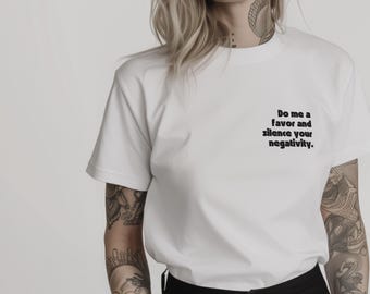May include: White t-shirt featuring the black text: "Do me a favor and silence your negativity". The t-shirt has a classic crew neck design.
