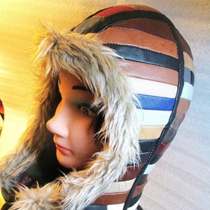 以下が含まれることがあります： ファーライニング付きのマルチカラーの革ジャケット。ジャケットは、異なる色の革のパネルを縫い合わせて作られています。フードは、厚いフェイクファーで裏打ちされています。