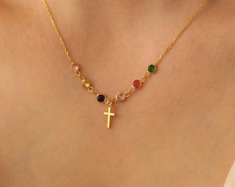 Puede incluir: Un collar de cadena dorada con un pequeño colgante de cruz y cuentas redondas de colores.