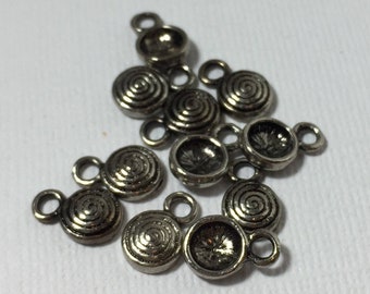 Puede incluir: Un grupo de abalorios de metal plateado con un diseño en espiral y un bucle para sujetar a joyas u otras manualidades.