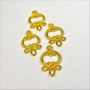 May include: Four gold-coloured metal charms with a circular design and a bow at the bottom. The charms are on a white surface.