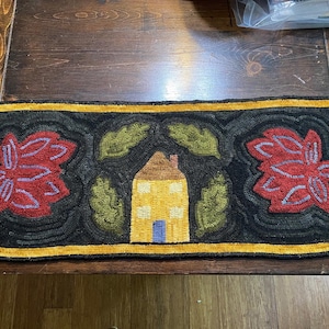 May include: A yellow house with a blue door and white windows is surrounded by green leaves and red flowers on a black background. The rug has a gold border.