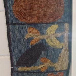 May include: A blue and brown rug with a pumpkin, a bird on a branch, and two flowers. The rug is made of wool and has a textured surface.