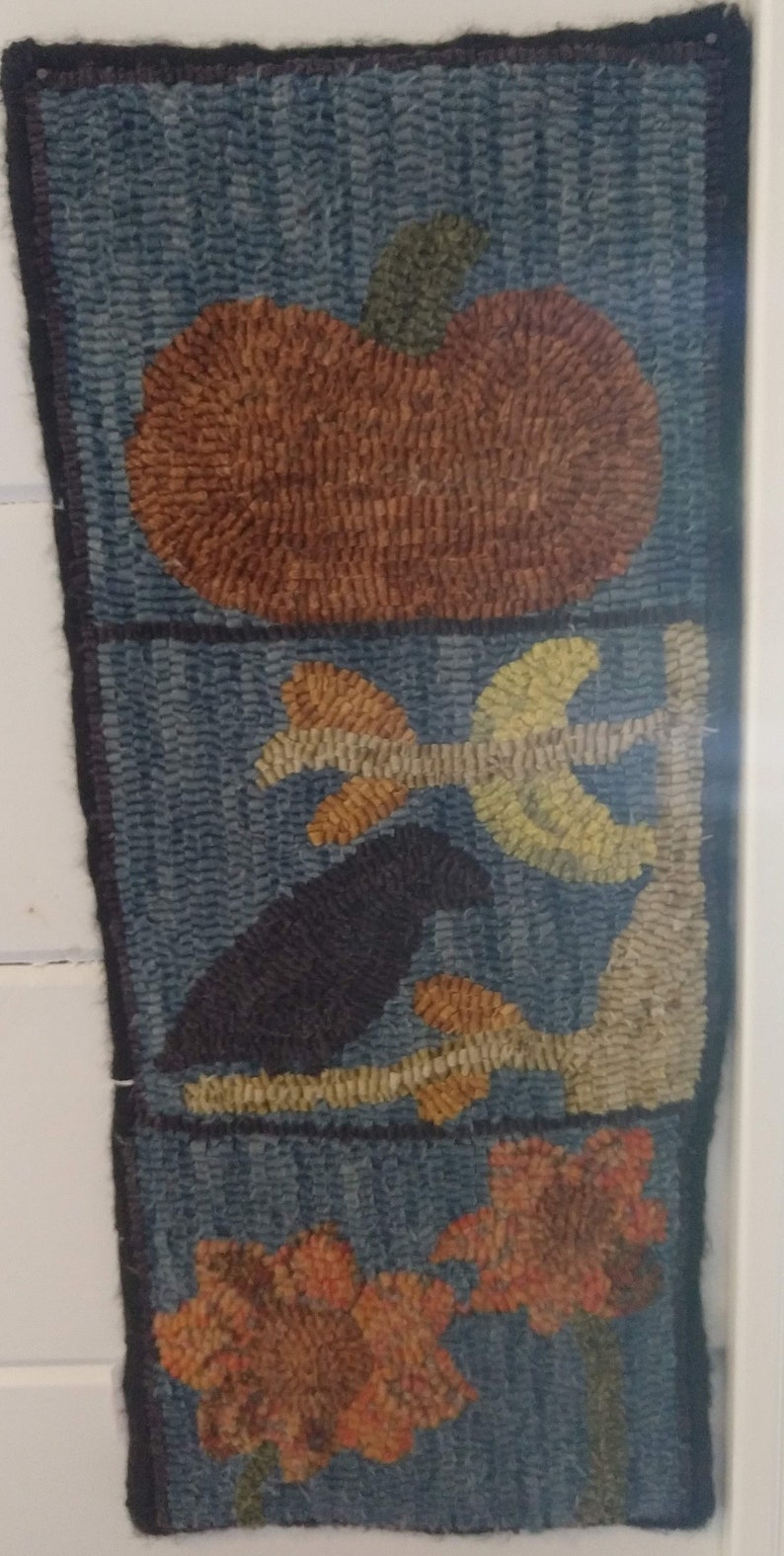 Puede incluir: Una alfombra azul y marr&oacute;n con una calabaza, un p&aacute;jaro en una rama y dos flores. La alfombra est&aacute; hecha de lana y tiene una superficie texturizada.