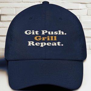 Puede incluir: Gorra de béisbol azul marino con la frase bordada "Git Push. Grill Repeat." El texto es blanco y dorado. La gorra tiene una visera curva y un botón en la parte superior.