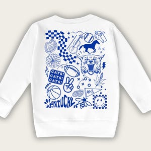May include: White sweatshirt with a blue graphic design featuring various sports and school-related icons. The word "KENTUCKY" is at the bottom, with "CATS!" repeated above. Other images include a horse, football, and basketball.