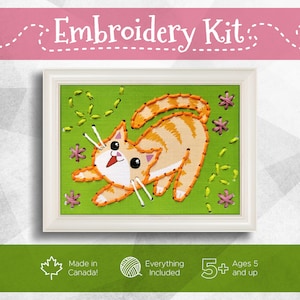 May include: Embroidery kit featuring a playful orange tabby cat design. The cat is embroidered on a green background with pink and yellow accents, framed in a white border. The kit includes everything needed and is suitable for ages 5 and up. Made in Canada.