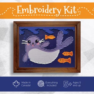 May include: An embroidery kit featuring a framed design of a purple seal swimming with orange fish against a blue background. The kit includes everything needed and is for ages 5 and up. The text "Embroidery Kit" is at the top.
