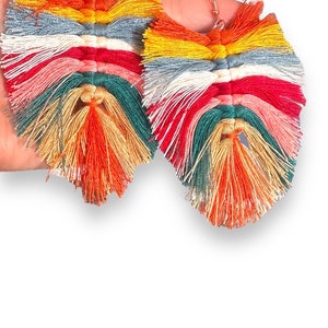 May include: A pair of colorful tassel earrings with a rainbow of colors including red, orange, yellow, green, blue, and pink. The tassels are made of yarn and are attached to silver hooks.