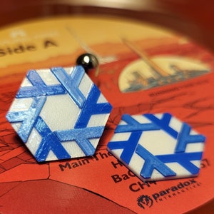 以下が含まれることがあります： 2つの六角形の白と青の幾何学模様が赤いレコードの上に置かれています。デザインは、青いクロスハッチパターンを持つ白い中心部が特徴です。レコードレーベルには「Side A」などのテキストが表示されています。