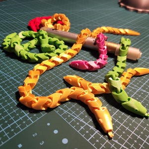 Könnte beinhalten: Ein Satz bunter, flexibler Kunststoffkettenglieder in Form von Schlangen. Die Ketten sind in den Farben Grün, Gelb, Pink und Rot.