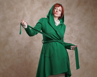 May include: A woman wearing a green hooded wrap dress with a long tie belt. The dress has a high-low hemline and a pocket on the front. She is wearing white knee-high boots.
