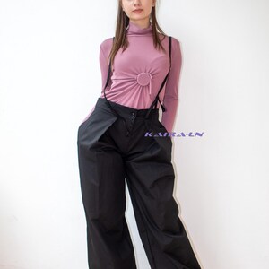 以下が含まれることがあります： 女性がピンクのタートルネックのシャツと、サスペンダー付きのワイドレッグの黒いパンツを着用しています。パンツはハイウエストでゆったりとしたフィット感です。