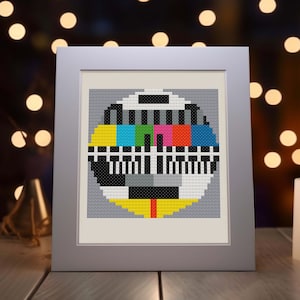 May include: A framed picture of a television test pattern, also known as a test card, made of colorful squares and black and white lines. The test pattern is in a silver frame.