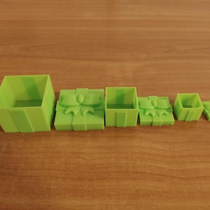 May include: A set of six lime green gift box moulds in different sizes. The boxes are arranged in a row, with the largest box on the left and the smallest on the right. Some boxes feature a bow design.