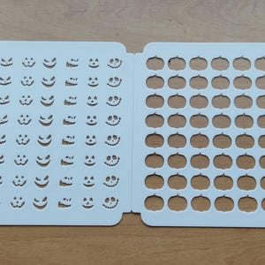 Puede incluir: Plantilla de plástico blanco con dos secciones. La sección izquierda tiene una cuadrícula de 9 filas y 8 columnas de caras de calabaza. La sección derecha tiene una cuadrícula de 9 filas y 8 columnas de formas de calabaza.